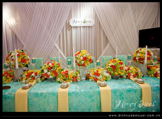 Hoa trên bàn uống nước của hai họ được chăm chút tỉ mỉ, công phu. Những bình hoa có sắc màu tươi tắn, được kết từ ba gam màu chủ đạo là xanh, vàng và cam hồng khiến không khí trẻ trung, hiện đại.